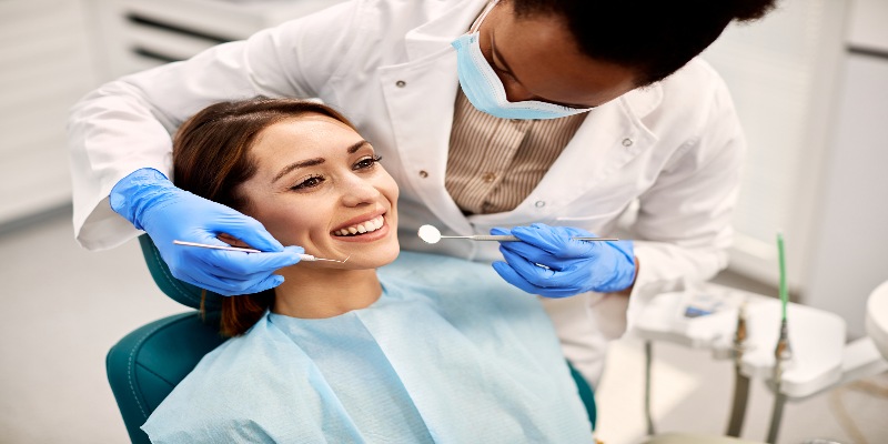 Una mujer sentada en un consultorio dental mientras un odontólogo revisa sus dientes.