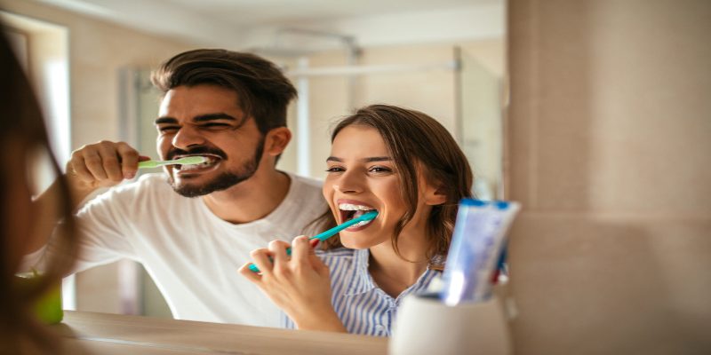 Una pareja cepillándose los dientes frente al espejo. 