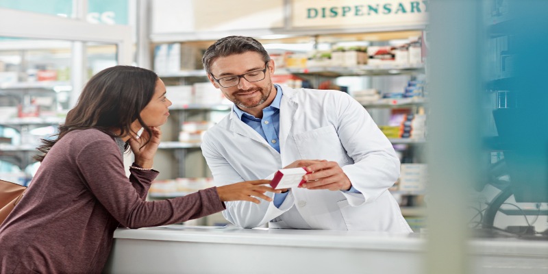 Mujer en una farmacia consultando con un farmacéutico sobre un medicamento.