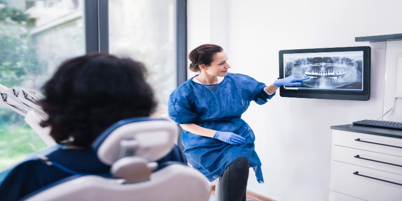 Odontóloga mostrando radiografías a paciente para implantes dentales en su consultorio.