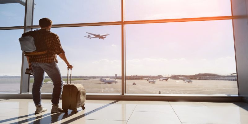 Hombre en un aeropuerto, mirando por la ventana mientras espera para embarcarse en su vuelo.